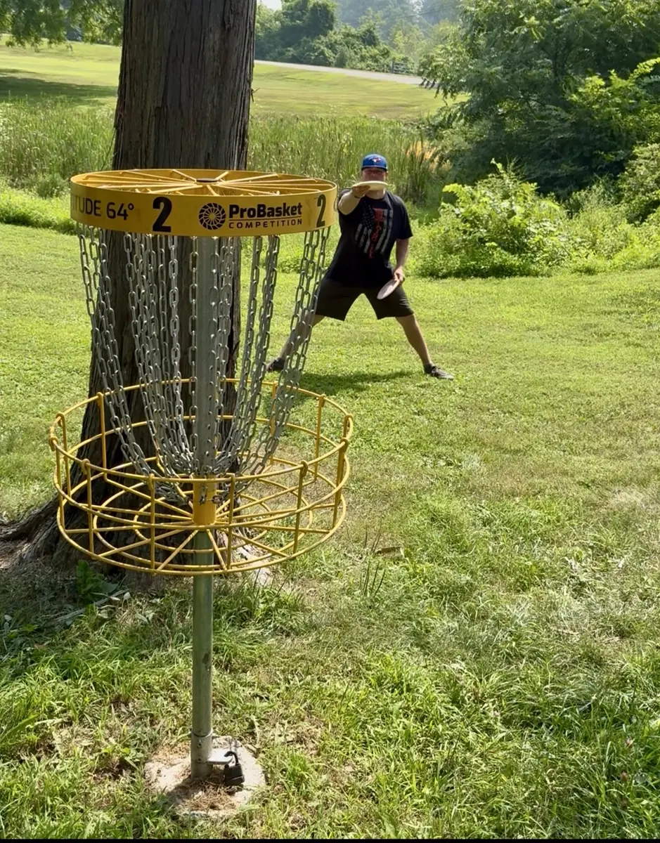Mike from BlueJayDG throwing beside a disc golf basket