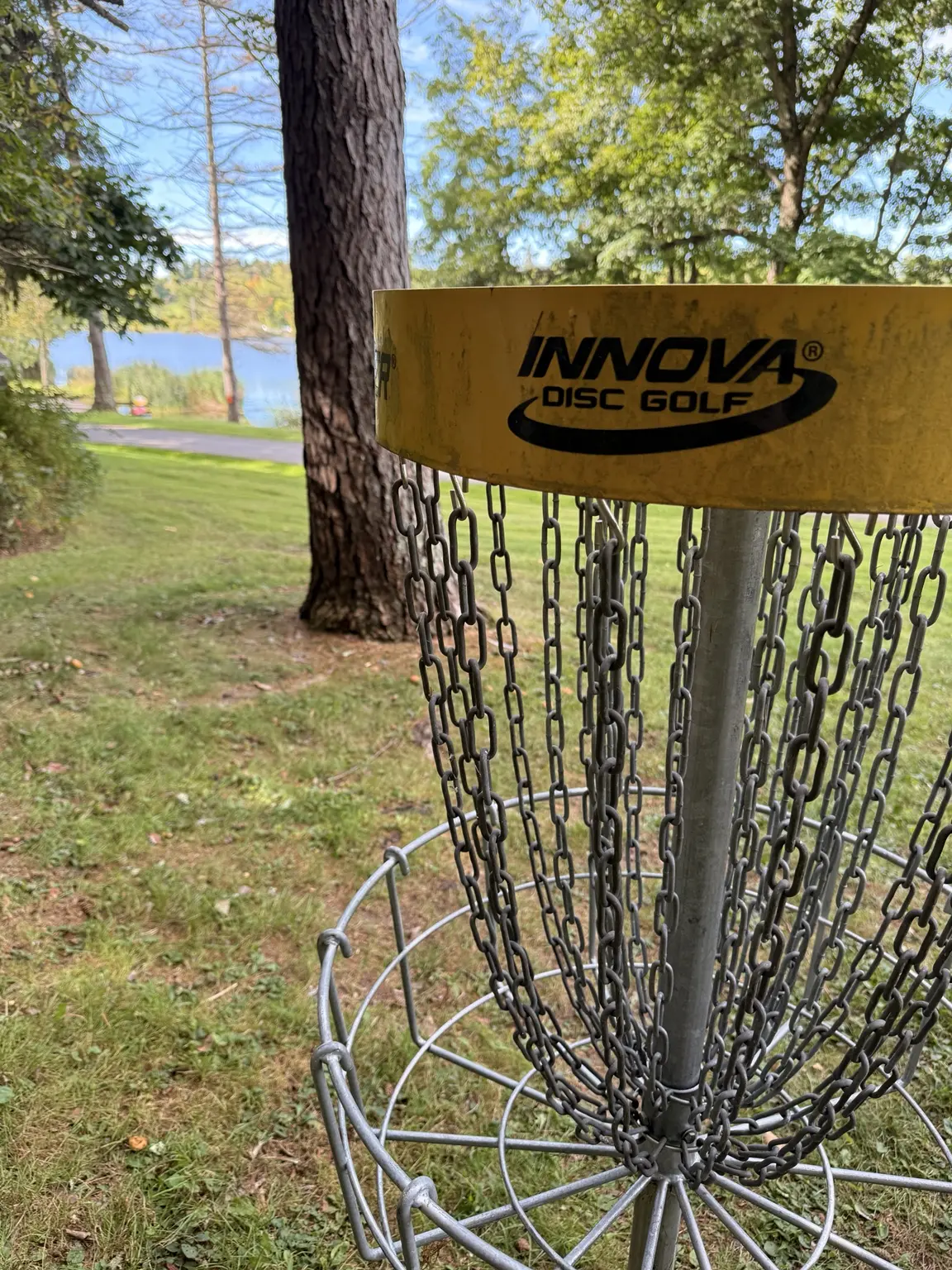 Disc golf basket beside a lake on a wooded course